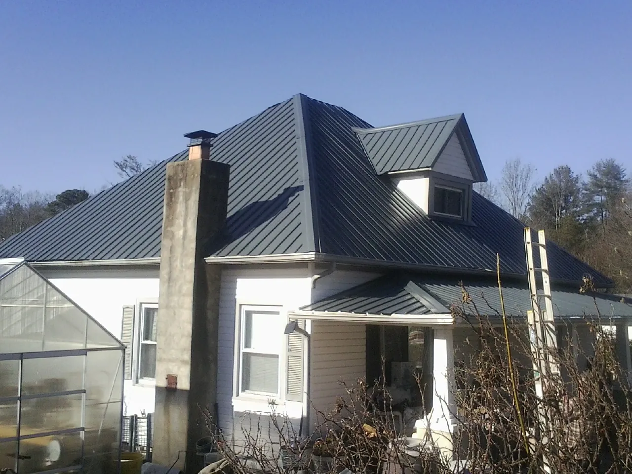 Dark blue standing seam metal roof on a white farmhouse with dormer — Slate & Tile Roof Repair by Roofing Brothers in Block Island