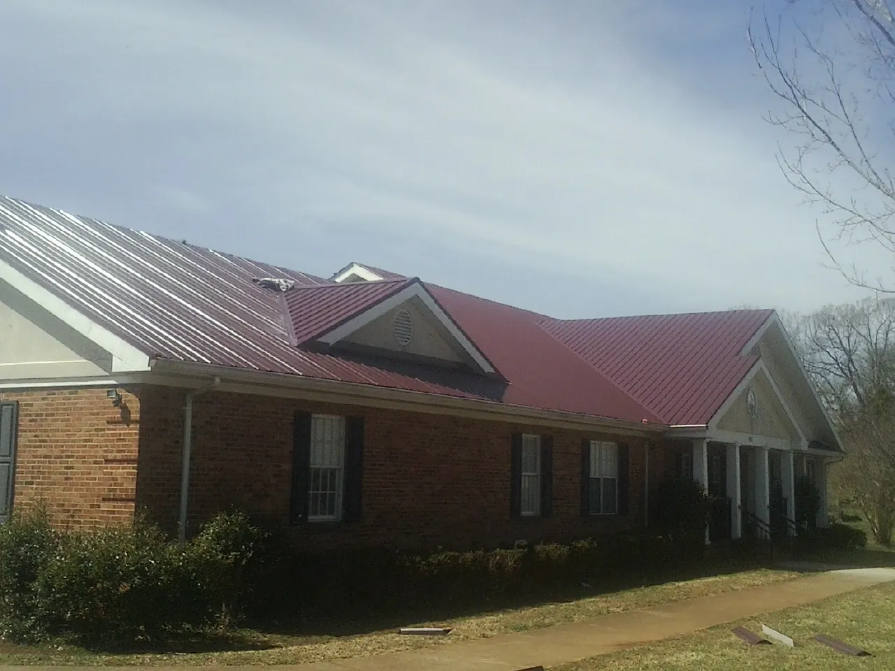 Red metal roof with gabled entries on a long brick building, from a Hail Damage Roof Repair job in Block Island