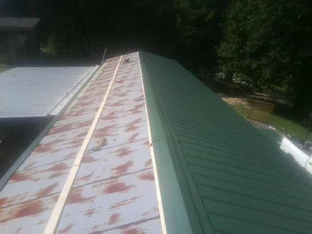 Old rusted panels beside newly installed green metal roofing — Wind Damage Roof Repair by Roofing Brothers in Block Island