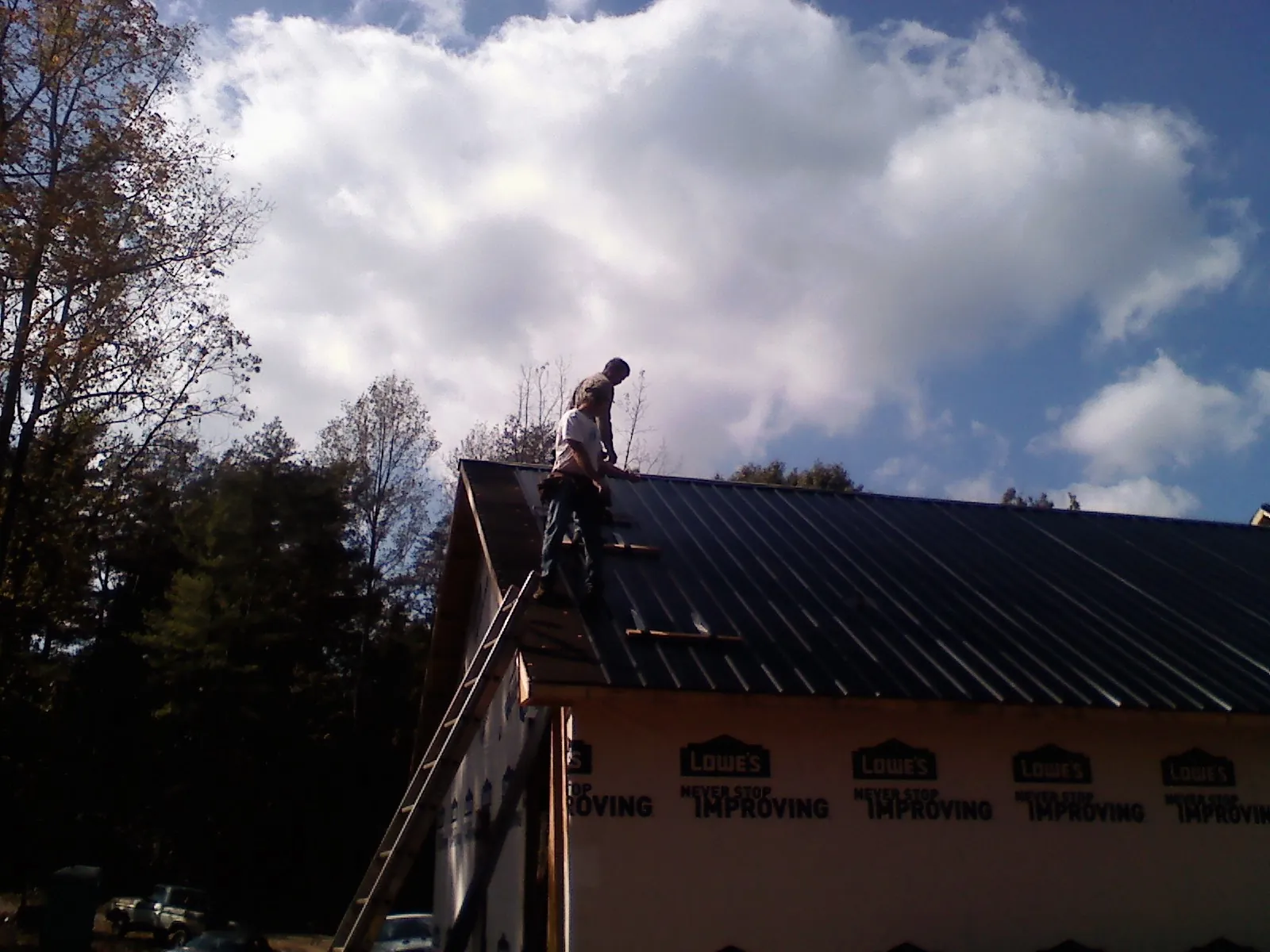 Roofer fastening dark metal panels high against a cloudy sky, from a Roof Inspection job in Block Island