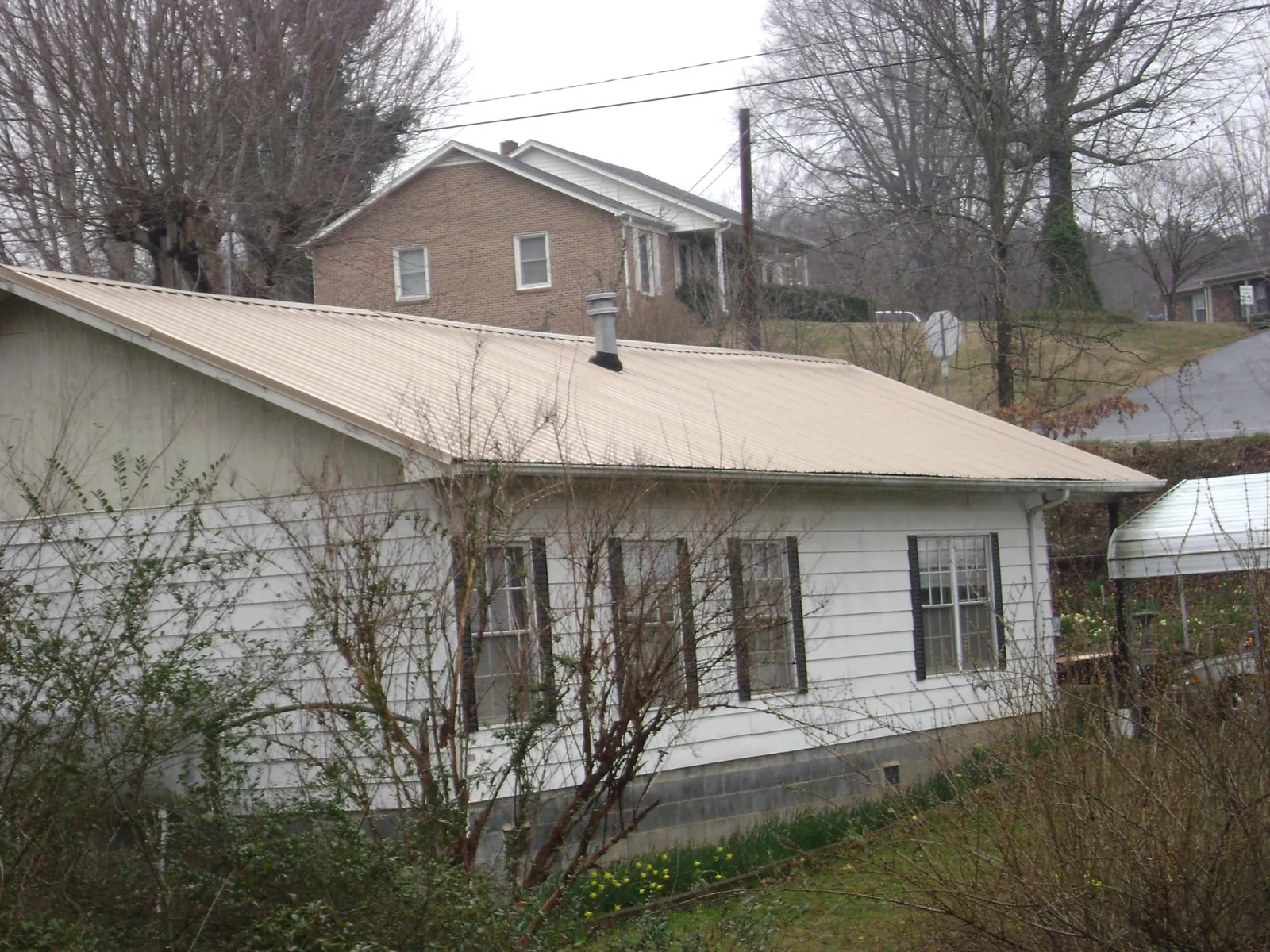 Tan metal roof on a white sided house set into a hillside — Commercial Roofing by Roofing Brothers in Block Island